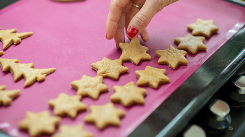 Hand placing small star-shaped cookies on silicone baking mat