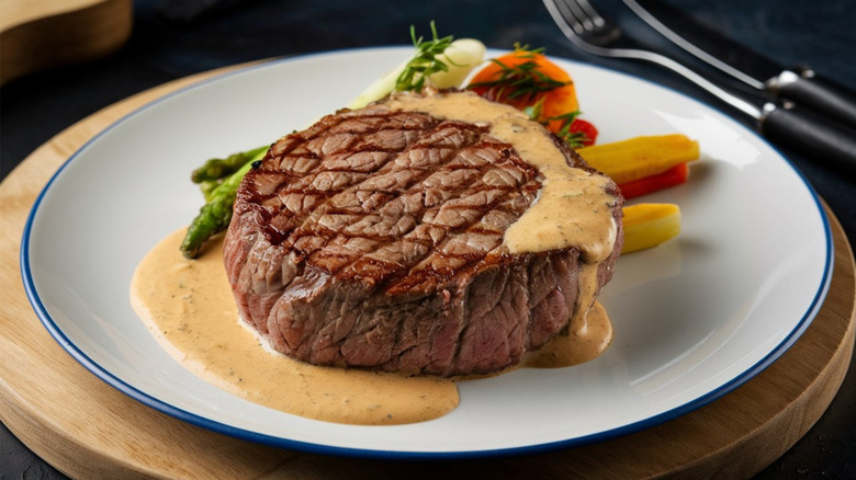 Fillet mignon with steak sauce and some vegetables on white plate