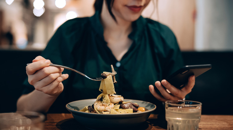 Person looking at phone whilst eating seafood meal in restaurant