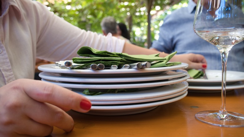 Person holding pile of stacked plates with cutlery and napkins on wooden table