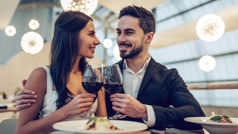 Young couple smartly dressed in restaurant holding glasses of red wine