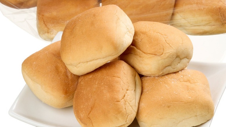 Five dinner rolls on plate in front of plastic bag of rolls