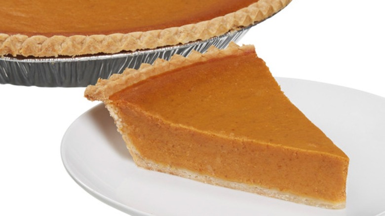 Slice of pumpkin pie on plate beside whole pie in baking tin