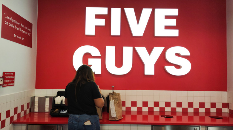 A Five Guys sign with a woman unpacking her order
