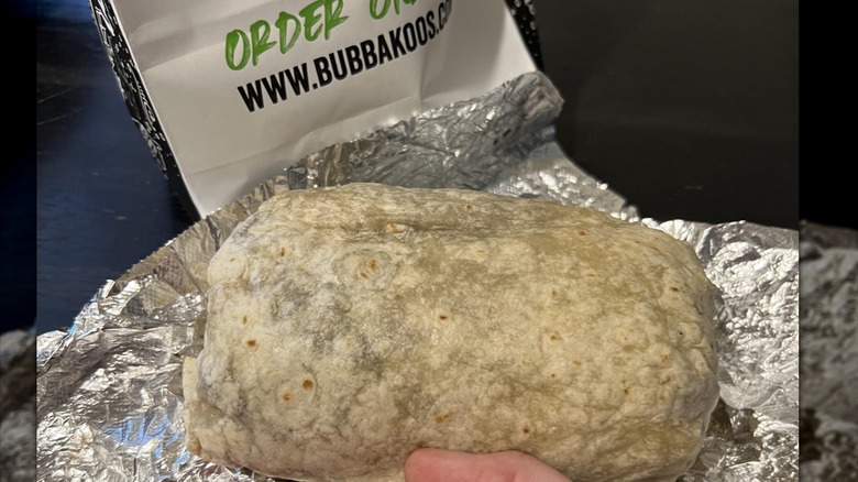 A massive burrito next to a Bubbakoos bag, sitting on foil