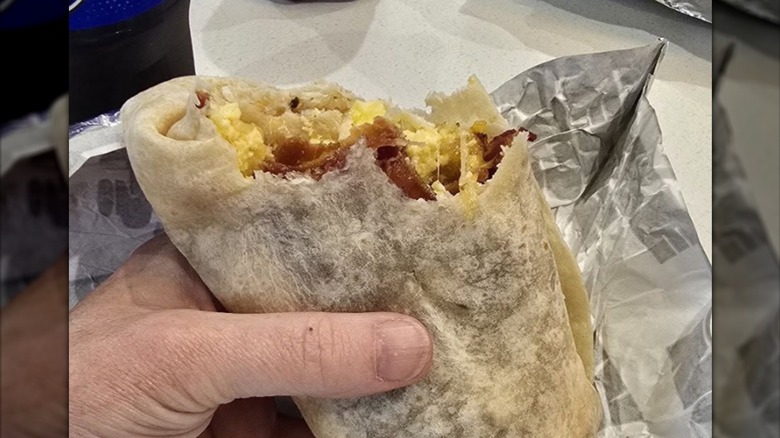 A hand holding a half-eaten breakfast burrito
