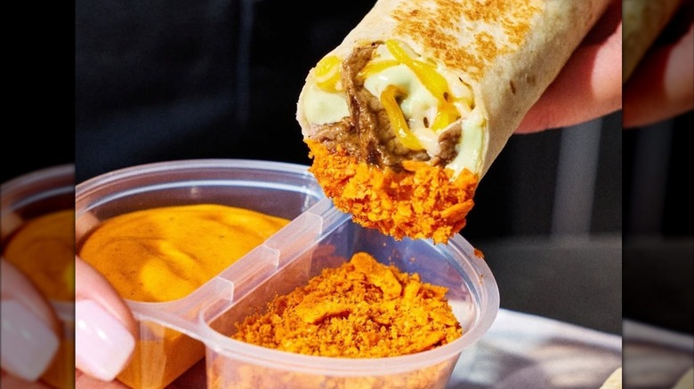 Someone dipping a burrito in crunchy cheese bits from a cup next to some sauce