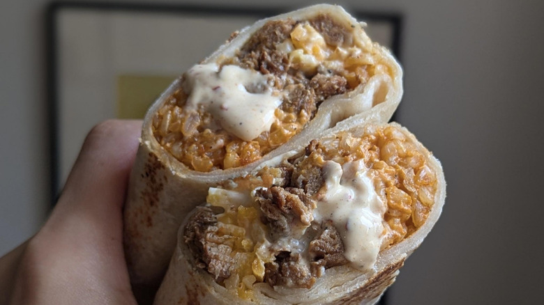 A person holding two halves of a Pepperjack Steak Burrito
