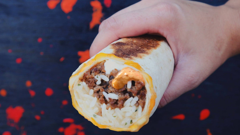 A person holding a Taco Bell Volcano Quesarito with beef, rice, and sauce visible inside