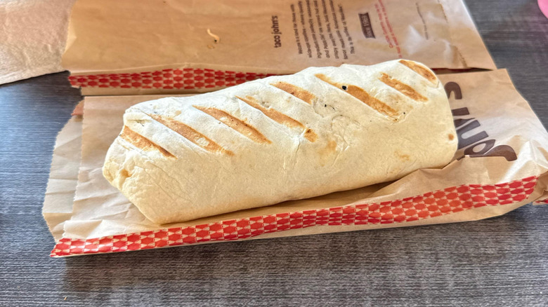 A large, grilled burrito sitting atop a paper bag on a table
