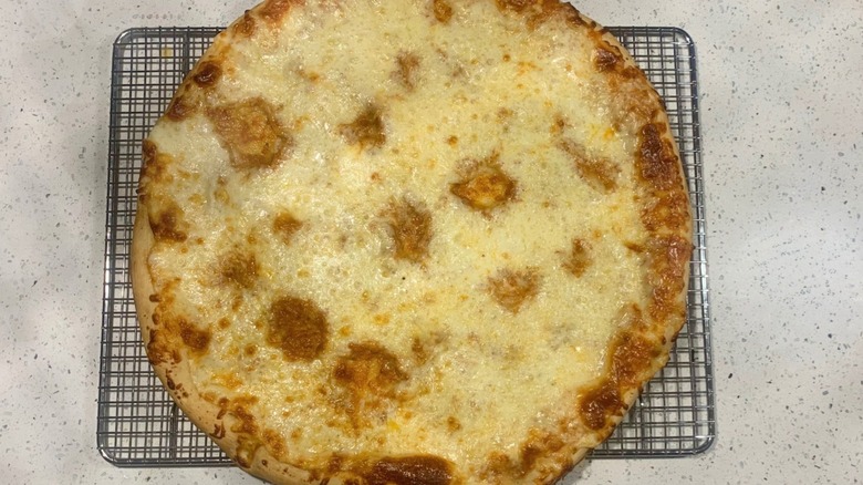 A plain pizza sits on a wire rack settled on a marble countertop