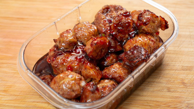 Grape jelly meatballs in a plastic container on a wooden table.
