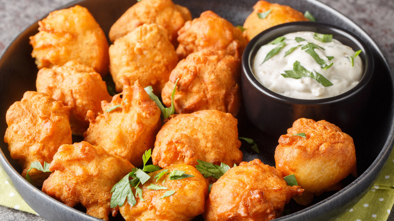 Hushpuppies with creamy dipping sauce in a black bowl.