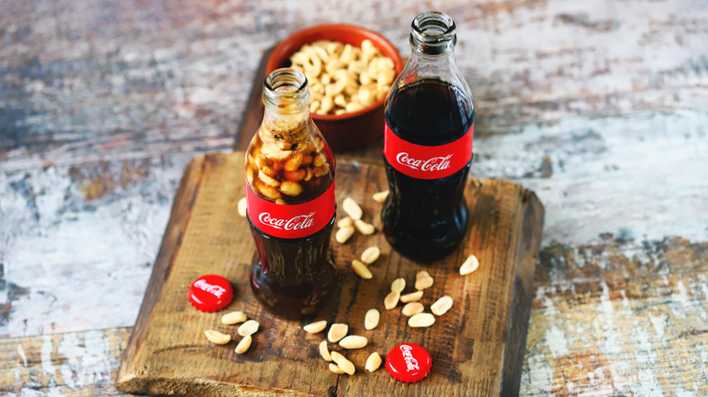 Coca-Cola glass bottles with peanuts on a wooden cutting board.