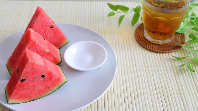 Sliced watermelon with a salt dish and glass of iced tea on the side.