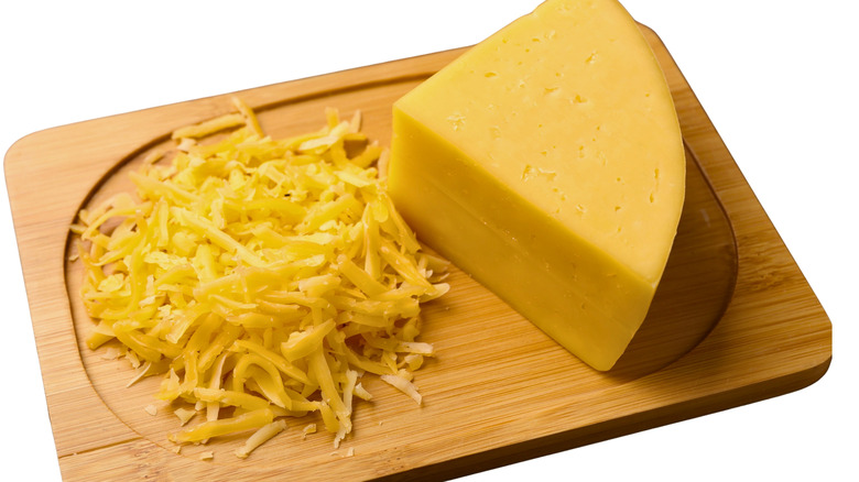 Block of cheese and shredded cheese on a cutting board