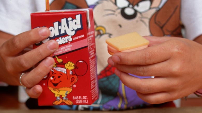 A school-age child holding a Kool-Aid juice box and a Lunchables