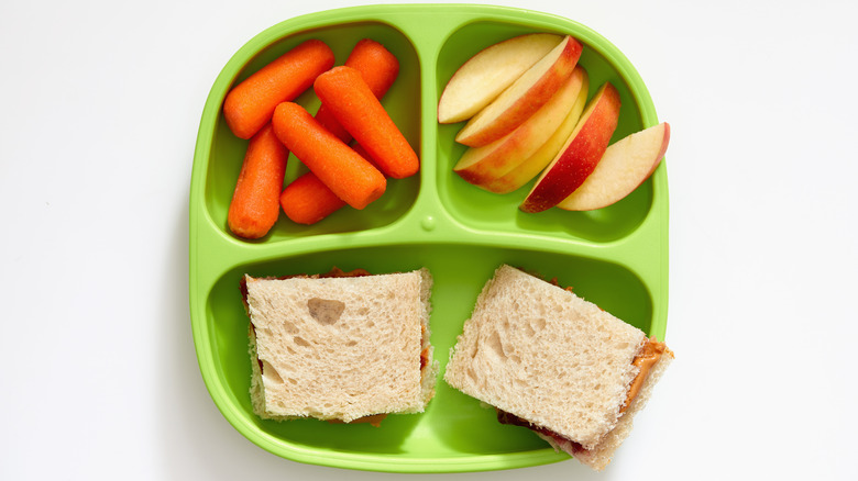 Baby carrots, apple slices, and a cut sandwich on a green plate