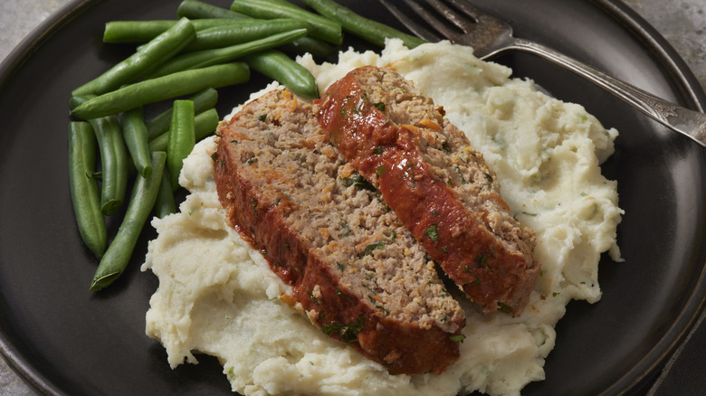 Plate of meatloaf, green beans, and mashed potatoes with a fork