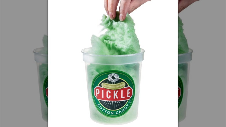 Plastic tub of pickle flavored cotton candy with hand pulling candy out of container