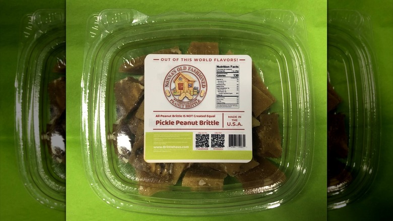 Plastic box of Nonna's Old Fashioned Peanut Brittle branded pickle peanut brittle candy on green surface