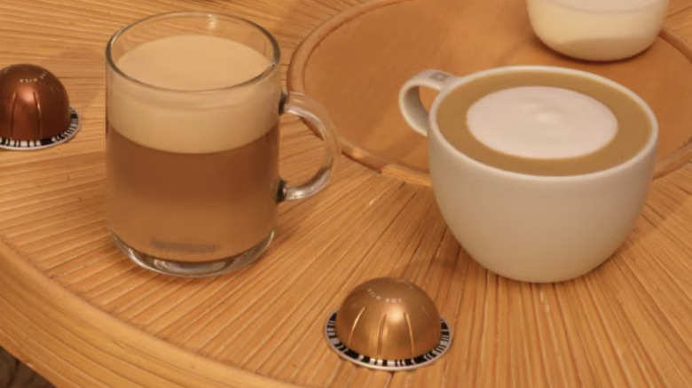 Coffees in mugs and two Nespresso pods on a round wooden table
