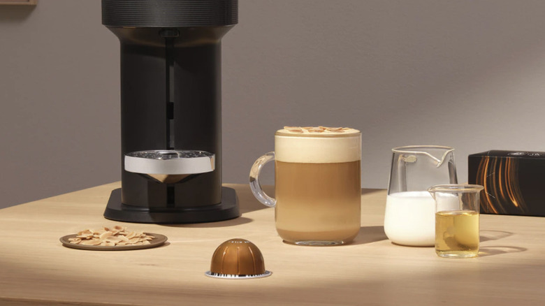 An Nespresso machine, mug of coffee, milk jug, and a Melozio Boost capsule on a wooden table