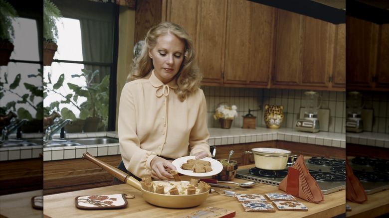 Woman in an '80s kitchen placing food on the plate from a pan