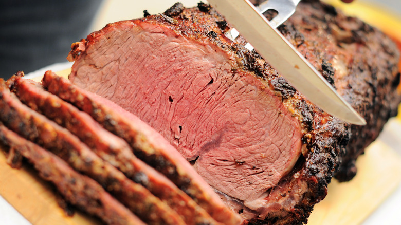 A piece of prime rib roast getting sliced, showing an an evenly cooked center