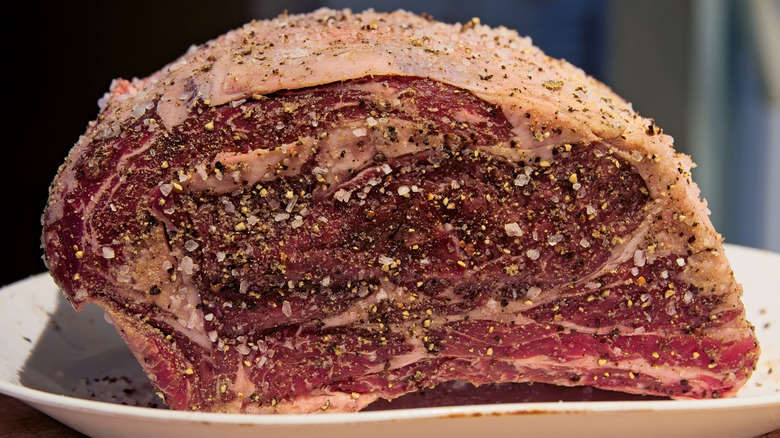 A raw prime rib roast covered in salt and pepper