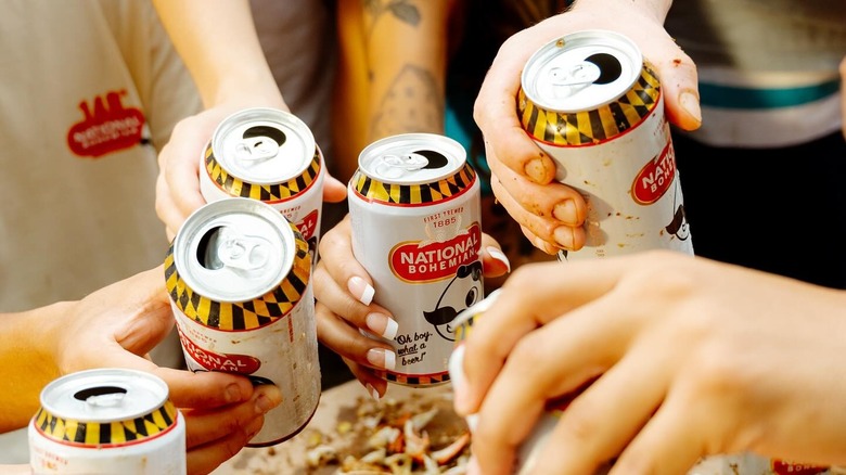 A group of people holding up opened cans of National Bohemian close together