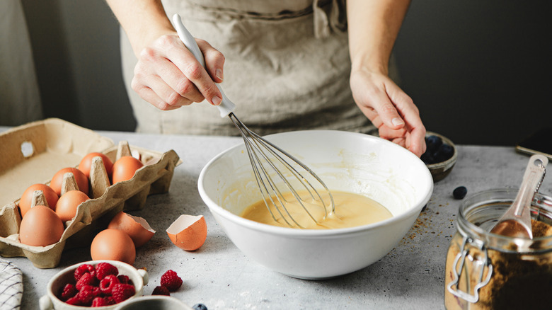 Person whisking eggs near baking ingredients