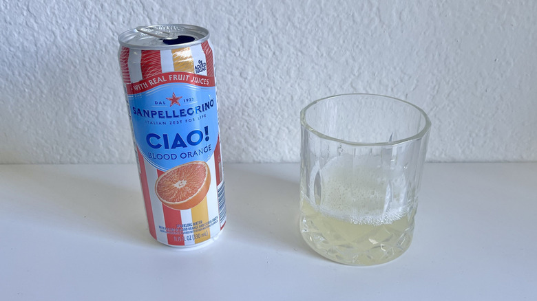 Ciao Blood Orange Sparkling Water in a glass with a can next to the glass on a white counter