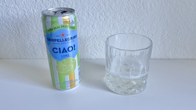 Can of Ciao Lime Sparkling Water next to a glass against a white wall
