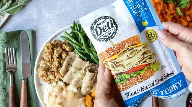 A hand holding Unreal Deli Roasted Turkey against several dinner ingredients