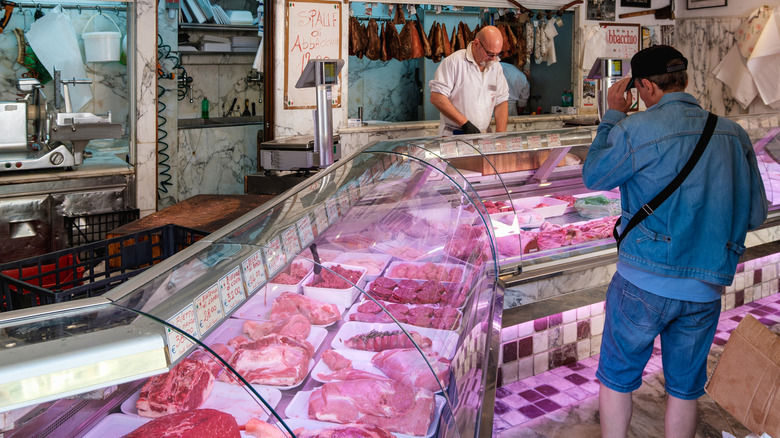 Person looking at the raw meat in display case at butcher shop.