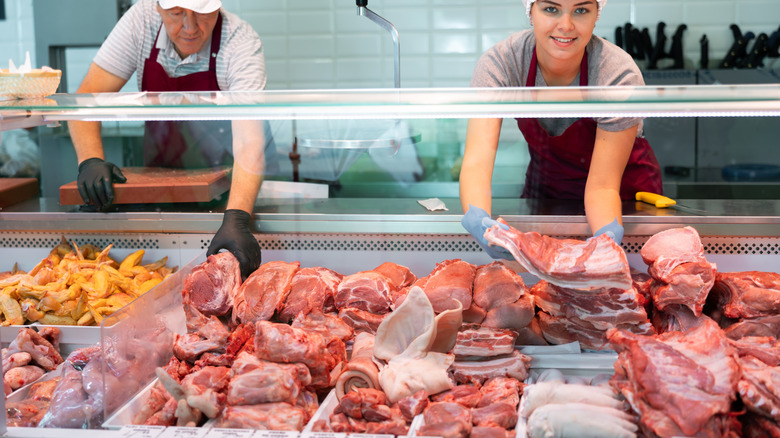 Two butchers behind counter sorting the meat in the display case.