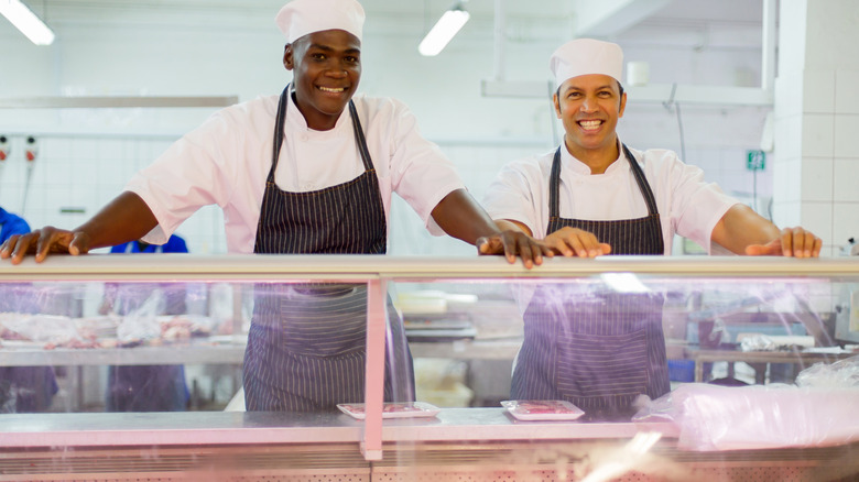 Two butchers standing behind meat display case smiling broadly.
