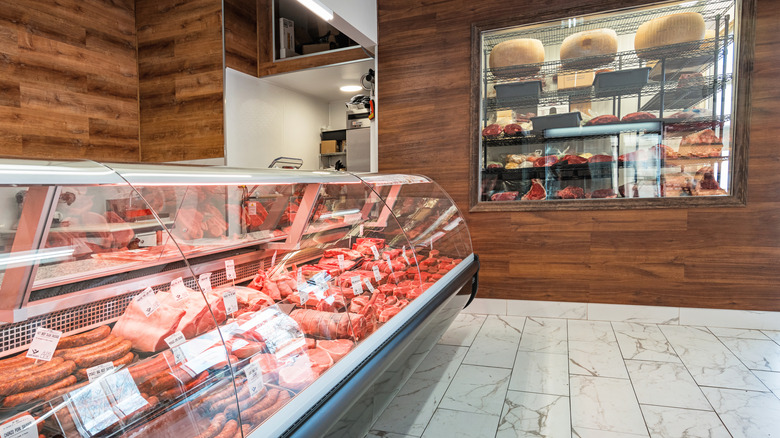 Interior of butcher shop with meat display case and cheese wheels in window display.