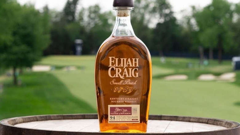 A bottle of Elijah Craig Small Batch placed on a barrel with a blurred golf course in the background
