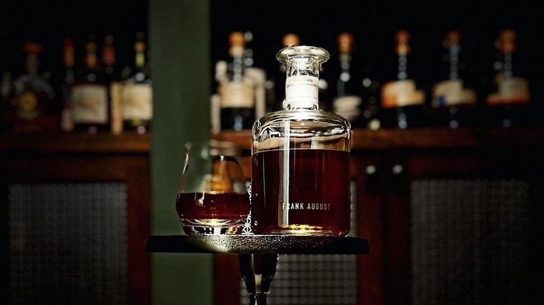 A bottle of Frank August Small Batch Bourbon placed on a small table next to a filled glass