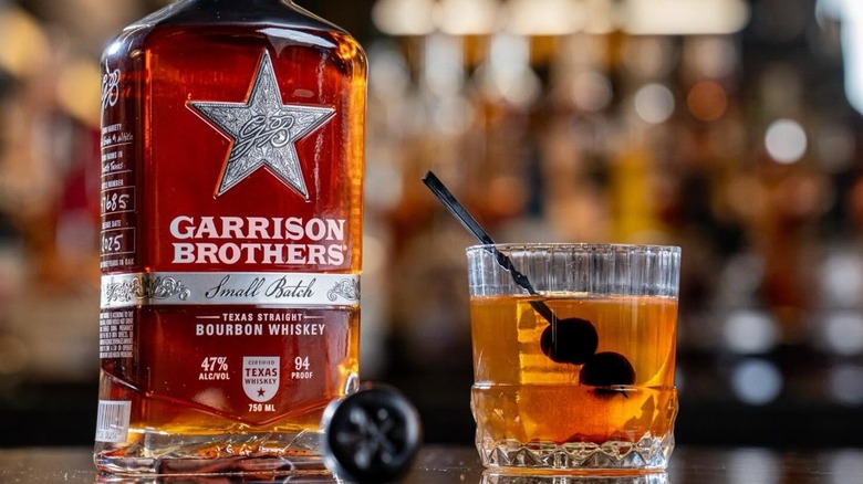 A close shot of a bottle of Garrison Brothers Small Batch Bourbon on  a bar next to a cocktail