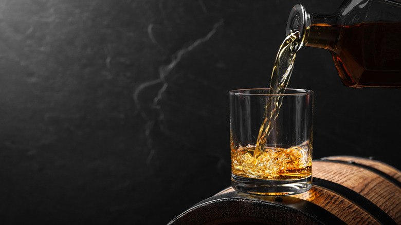 Whiskey being poured into a glass as it sits on top of a small barrel