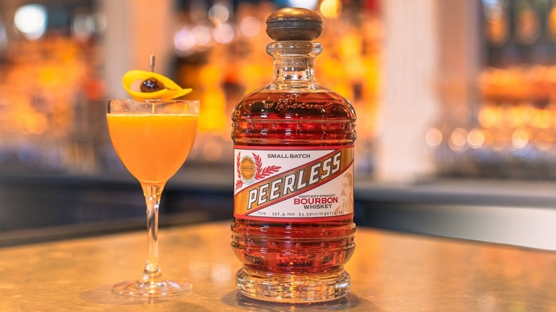 A bottle of Kentucky Peerless Small Batch Bourbon placed on a table next to a cocktail