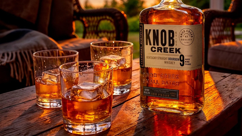 A bottle of Knob Creek 9-year placed on a table outdoors next to three filled glasses