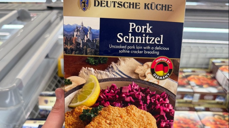 A hand holding a box of Aldi's Deutsche Küche frozen pork schnitzel above an island freezer