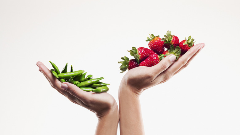 A pair of hands weighing green beans against strawberries