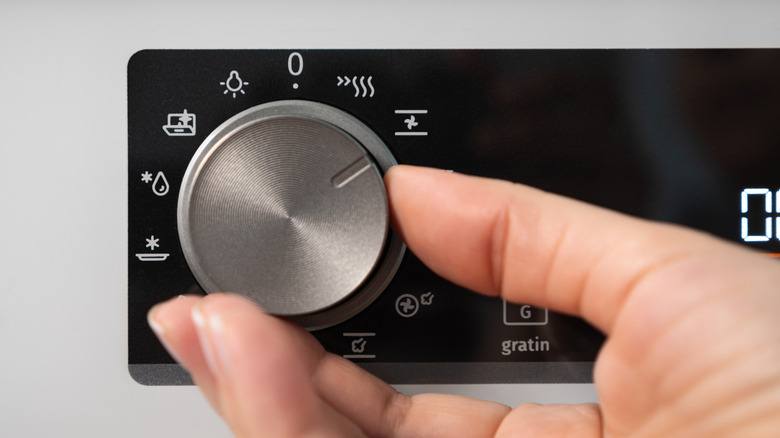 A hand turning the settings dial on an oven