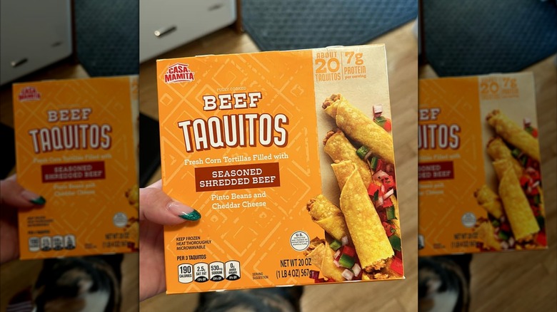 A hand holding a box of Casa Mamita beef taquitos
