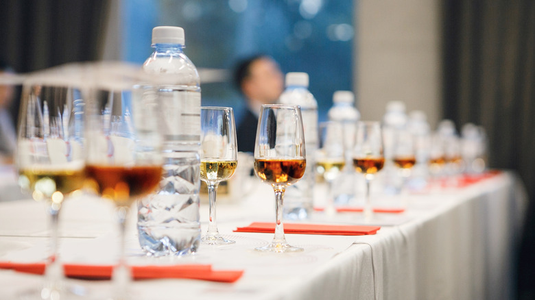 Many glasses of whiskey lined up for a tasting session with a bottle of water shown at each station
